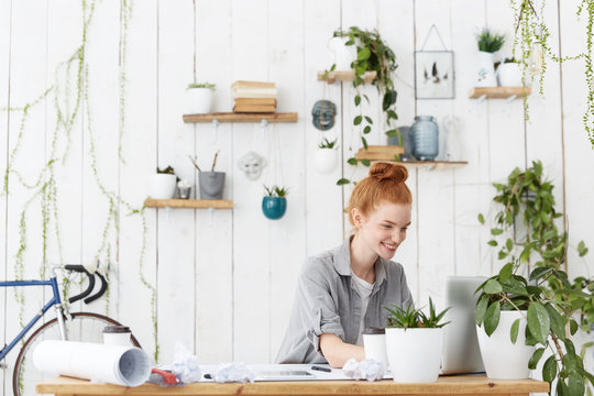 Cheerful Positive Young Redhead Woman Designer With Hair Bun Making 3d Interior Design Using Cad System On Laptop Computer, Enjoying Process Of Creation, Looking At Screen With Excited Smile