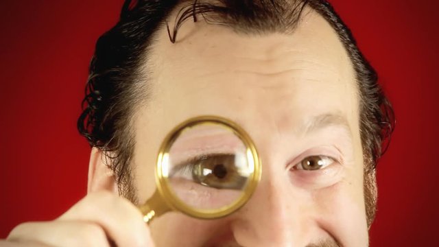 A funny ugly man looking at the camera with a magnifying lens (parody of a spy), searching for valued information.
