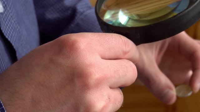 numismatist considers old coins through magnifying glass.