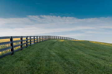 Black Fence Leads Over Grassy Hill