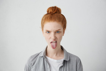 Headshot of naughty girl of European appearance sticking out tongue, trying to tease someone, looking immature and offensive, all her appearance expressing rudeness and disgust. Signs, symbols