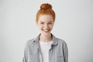 Beautiful ginger freckled girl with mysterious smile posing indoors at blank grey studio wall....