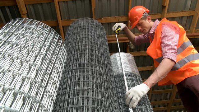 The worker measures with a tape measure the width of the iron grid