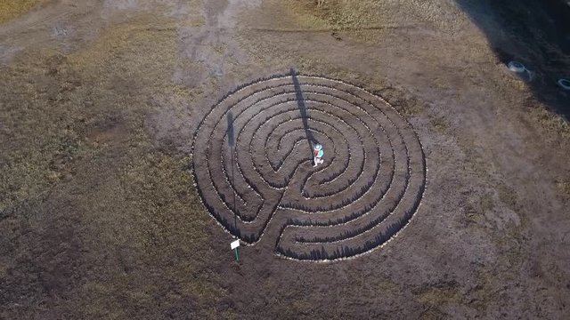 Aerial orbit of a woman walking a labyrinth in a park