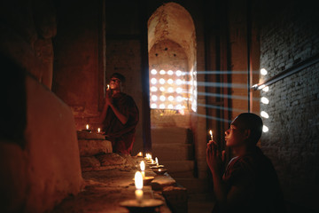 Obraz na płótnie Canvas Novices praying with candles in front of buddha statue inside old pagoda, Bagan Myanmar