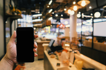 man holding smartphone with blank screen in the front of blurred restaurant background for reserve online; payment; coworking space conceptual.