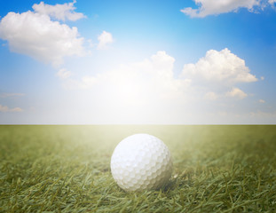 golf ball on fake green grass with sunlight and cloud blue sky background.
