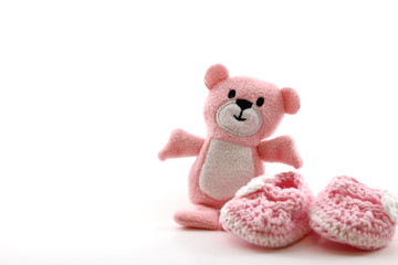 A photo of a teddy bear and pink baby booties isolated on a white background