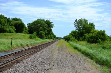 Fototapeta na wymiar Railroad tracks on a green and rural summer countryside