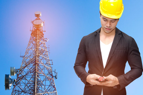 Smart Construction Manager With Walkie-talkie Or Two Way Radio In Hand And Yellow Safety Helmet With Telecommunication Tower With Blue Sky Background, Technology, Business And Industrial Concept.