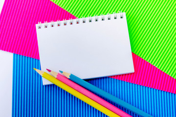 Blank  spiral notepad and colorful pencils on green, pink and blue corrugated cardboard paper . Space for text or message