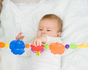 Baby girl playing with toy rattle lying on back