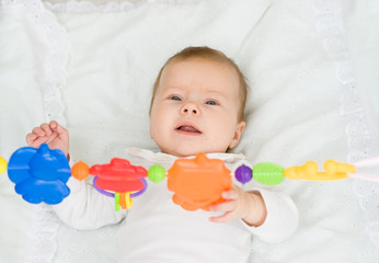 Happy newborn baby girl playing with toy rattle lying on back