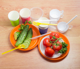 Disposable cutlery and several vegetable on wooden surface