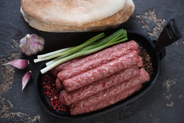 Raw cevapi or skinless beef sausages on a dark brown stone background, high angle view