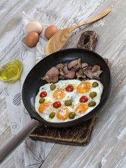 fried eggs with bacon, olives and tomatoes a hearty breakfast. 