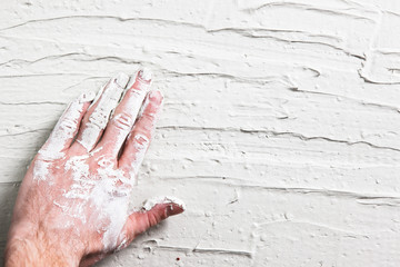 Repair background, flat lay of white plaster wall with worker hand. Rough grungy backdrop with free space for text.