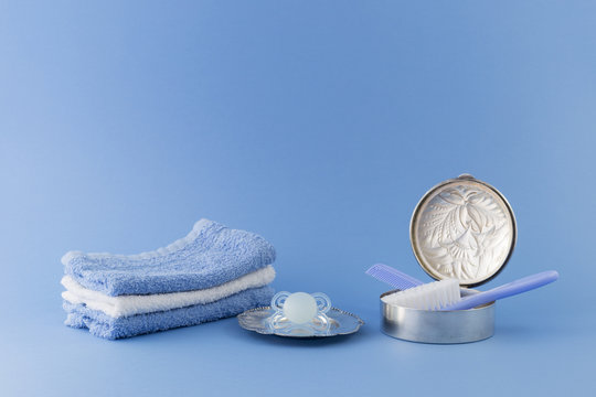 Baby boy luxurious items collection isolated on pale blue background. Silver can with hairbrush and comb. Pacifier on a silver plate, towels.