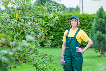 professional gardener at work. smiling young woman pruning apple tree in the yard. garden worker trimming plants. gardening service, horticulture and business concept