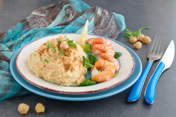 Chickpea puree with cream and butter served with boiled prawns on a white and blue plate on a grey abstract background. Healthy food. Healthy eating concept