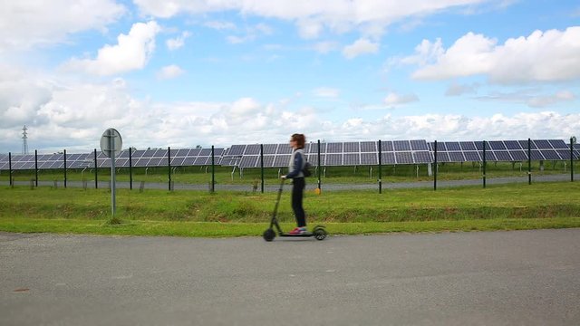 Girl riding An Electric Kick Scooter - Solar Panels in the Background