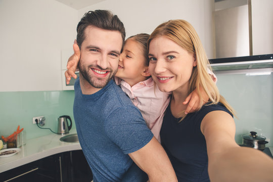 Young family smiling taking pictures together in kitchen