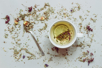 Tea background. Dry herbal tea and cup of hot tea with spoon on the gray background