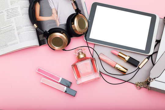 Perfume, lip gloss, lipstick and gold headphones on a pink background