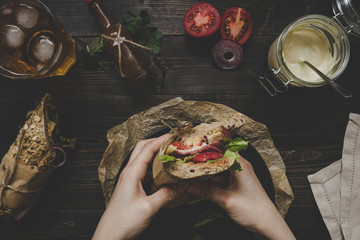 Hands holding fresh delicious submarine sandwiches on the wooden table. Top view