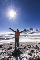 man standing with hands up near ojos del salado volcano in chile