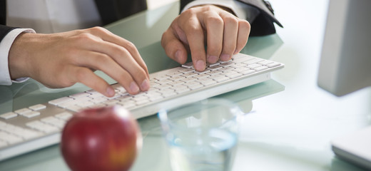 Geschäftsmann tippt auf Tastatur mit Apfel und Glas Wasser