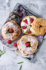 Homemade choux pastry cake Paris Brest with raspberries, almond, sugar powder and rosemary, served on wooden serving tray over gray blue texture background. French dessert. Top view