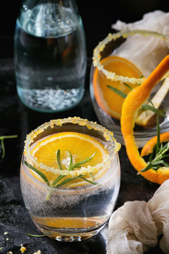 Tonic water cocktail with rosemary and orange. Two glasses and bottle with zest sugar and bubbles over black texture background. Refreshing beverage alco non alcohol. Close up