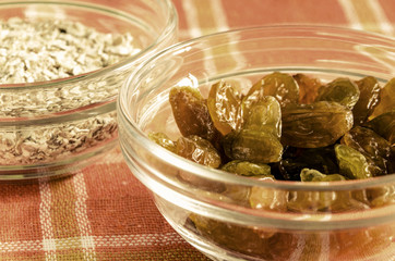 Oat flakes and raisins in a glass bowl on colorful dishcloth. Closeup shot. Healthy food concept. Toned.