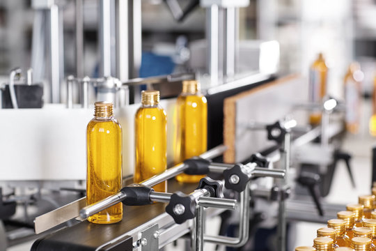 Factory and research concept. Bottles with yellow thick substance standing on manufacturing facility going to be twisted. Glass bottles in line on conveyor belt. Production process of cosmetics