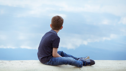 Child sitting on a pier lookinf at blue water
