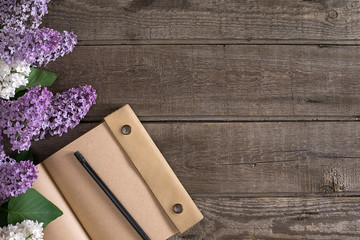 Fototapeta premium Lilac blossom on rustic wooden background with notebook for greeting message. Top view