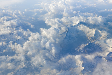 Sky scenery. Aerial view over the cumulus clouds and mountain peaks covered with snow on a sunny day. Swiss Alps.