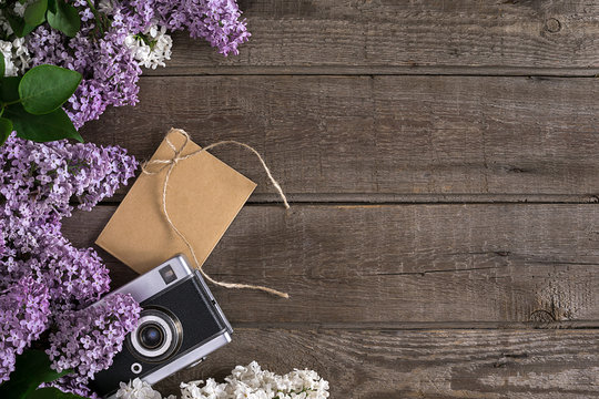 Lilac blossom on rustic wooden background with empty space for greeting message. Camera, small envelope. Top view