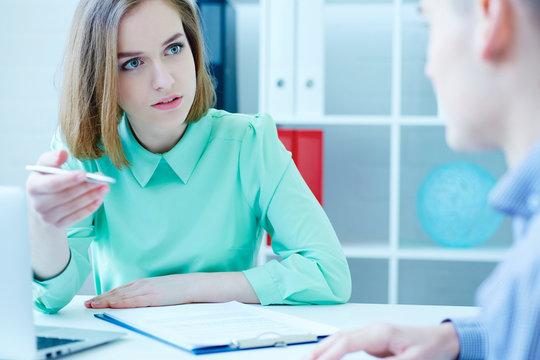 Young female employee of the staffing agency helps fill out the form to the male job seeker. Business, office, law and legal concept.