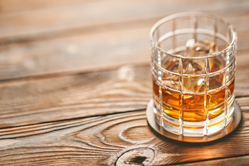 Glass of whiskey with ice cubes on wooden table