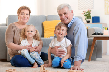 Happy senior couple and their grandchildren sitting on floor at home