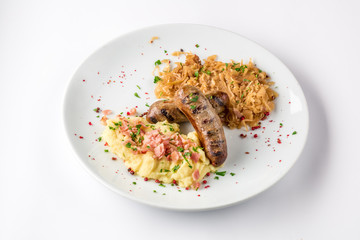 Grilled sausages, potatoes and braised cabbage on white plate close-up view from above.