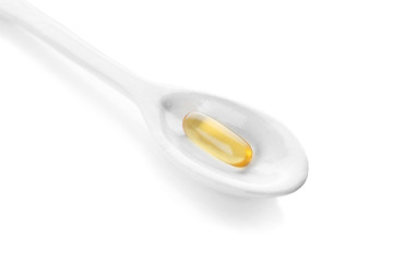Spoon with fish oil capsule on white background