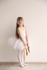 Beautiful little ballerina holding ballet shoes in light dance studio