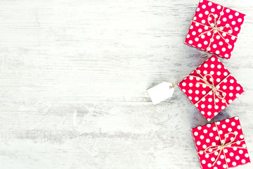 Empty card tied over red dotted gift box. Red dotted gift boxes over white wood background. Copy space.