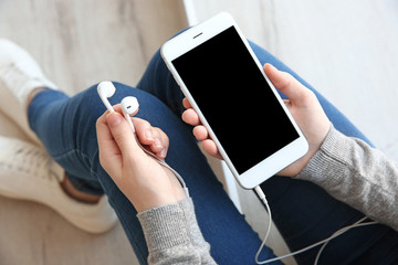 Audio book concept. Young woman holding smart phone and earphones, close up