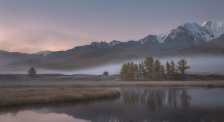 Misty autumn morning, a picturesque mountain lake on a background of snow capped mountains