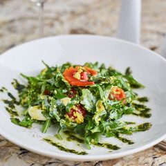 Salad with couscous, cherry tomatoes, avocado and mozzarella served on white plate. Salt shaker, pepper-castor and knife and fork on napkin on marble table
