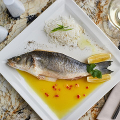 Whole boiled wolffish served with sauce from lemon butter and white wine on square white plate